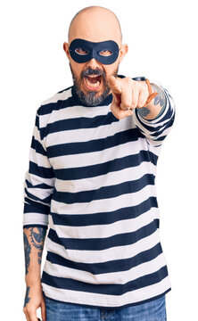 Young handsome man wearing burglar mask pointing displeased and frustrated to the camera, angry and furious with you