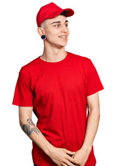 Fototapeta premium Young caucasian boy with ears dilation wearing delivery uniform and cap looking away to side with smile on face, natural expression. laughing confident.