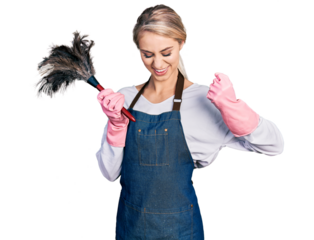 Beautiful young blonde woman wearing apron holding cleaning duster very happy and excited doing winner gesture with arms raised, smiling and screaming for success. celebration concept.