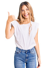 Beautiful caucasian woman with blonde hair wearing casual white tshirt smiling doing phone gesture with hand and fingers like talking on the telephone. communicating concepts.