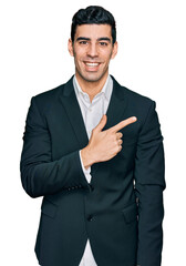 Handsome hispanic man wearing business clothes cheerful with a smile on face pointing with hand and finger up to the side with happy and natural expression