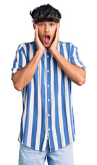 Young hispanic man wearing casual clothes afraid and shocked, surprise and amazed expression with hands on face