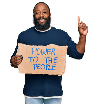 Young african american man holding power to the people banner surprised with an idea or question pointing finger with happy face, number one