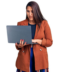 Young beautiful brunette woman using laptop thinking attitude and sober expression looking self...