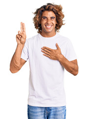 Young hispanic man wearing casual white tshirt smiling swearing with hand on chest and fingers up, making a loyalty promise oath