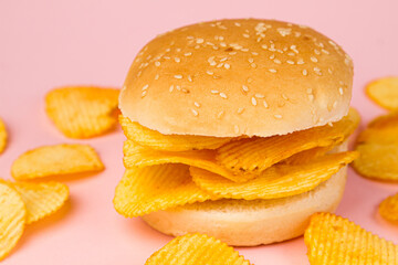 Hamburger with ribbed chips on a pink background.