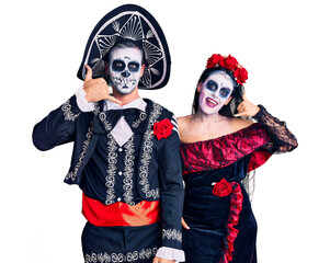Young couple wearing mexican day of the dead costume over background smiling doing phone gesture with hand and fingers like talking on the telephone. communicating concepts.