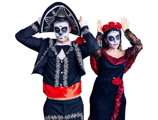 Young couple wearing mexican day of the dead costume over background doing bunny ears gesture with hands palms looking cynical and skeptical. easter rabbit concept.