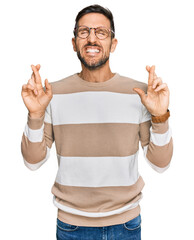 Handsome man with beard wearing casual clothes and glasses gesturing finger crossed smiling with hope and eyes closed. luck and superstitious concept.