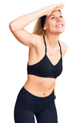 Fototapeta premium Young beautiful blonde woman wearing sportswear very happy and smiling looking far away with hand over head. searching concept.