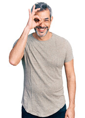Middle age hispanic with grey hair wearing casual grey t shirt doing ok gesture with hand smiling, eye looking through fingers with happy face.