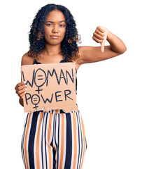 Young african american girl holding woman power banner with angry face, negative sign showing...