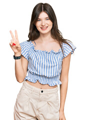 Young beautiful caucasian girl wearing casual clothes smiling looking to the camera showing fingers doing victory sign. number two.