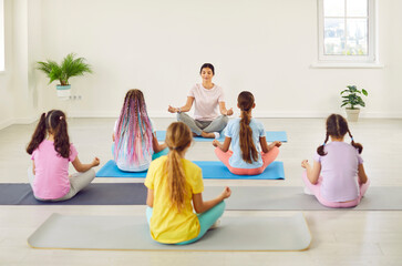Teenage kids girls sitting back on the floor with female teacher couch or trainer relaxing in gym sitting on yoga mat in Lotus pose meditating and doing yoga exercise. Children sport workout concept.