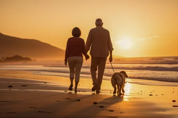 Poster An older retired couple walking their pet dog along a deserted beach at sunset © robert