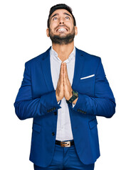 Young hispanic man wearing business jacket begging and praying with hands together with hope...