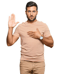 Handsome hispanic man wearing casual clothes swearing with hand on chest and open palm, making a...