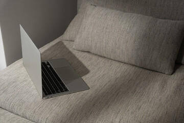 Laptop computer on comfortable sofa in sunlight shadows. Minimal modern styled interior design....