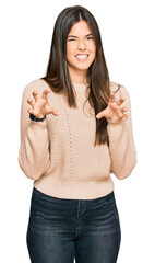 Young brunette woman wearing casual winter sweater smiling funny doing claw gesture as cat,...