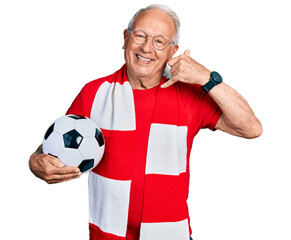 Senior man with grey hair football hooligan holding ball smiling doing phone gesture with hand and...