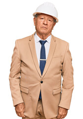 Senior caucasian man wearing architect hardhat with serious expression on face. simple and natural looking at the camera.
