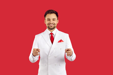Hey you. Handsome successful happy man smiling and pointing fingers at you isolated on red studio...