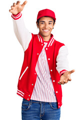 Young african amercian man wearing baseball uniform looking at the camera smiling with open arms for hug. cheerful expression embracing happiness.