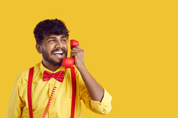 Telephone communication. Portrait of joyful Indian guy talking on retro phone, isolated on orange...