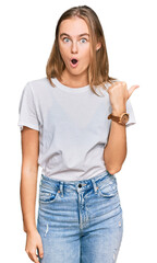 Obraz premium Beautiful young blonde woman wearing casual white t shirt surprised pointing with hand finger to the side, open mouth amazed expression.