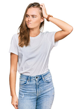 Beautiful young blonde woman wearing casual white t shirt confuse and wondering about question. uncertain with doubt, thinking with hand on head. pensive concept.