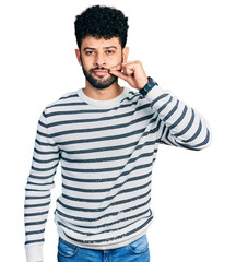 Young arab man with beard wearing casual striped sweater mouth and lips shut as zip with fingers....
