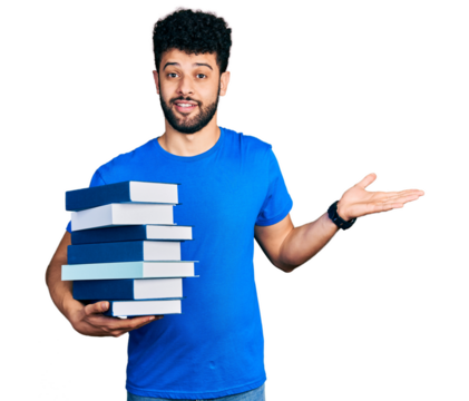 Young arab man with beard holding a pile of books celebrating achievement with happy smile and winner expression with raised hand - Powered by Adobe