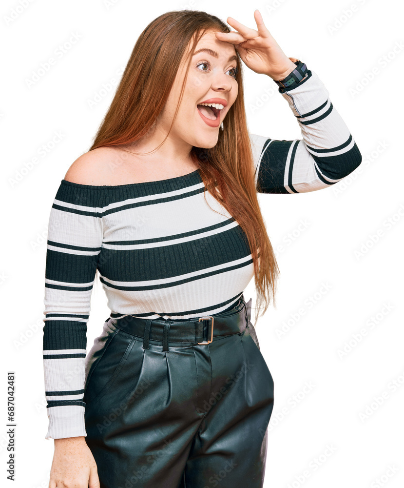 Wall mural Young beautiful redhead woman wearing elegant clothes very happy and smiling looking far away with hand over head. searching concept.