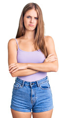 Young beautiful blonde woman wearing casual style with sleeveless shirt skeptic and nervous, disapproving expression on face with crossed arms. negative person.