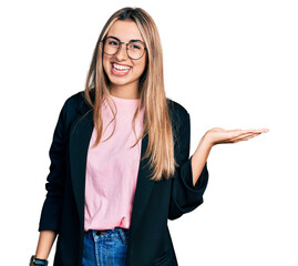 Hispanic young woman wearing business jacket and glasses smiling cheerful presenting and pointing...