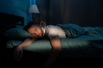 Sleepless caucasian man lying in bed at night suffering from insomnia. People, bedtime and rest - obrazy, fototapety, plakaty
