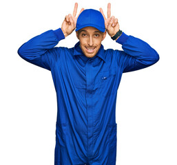 Bald man with beard wearing builder jumpsuit uniform posing funny and crazy with fingers on head as bunny ears, smiling cheerful