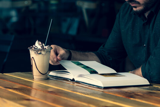 Young Guy Is Sitting At A Coffee House And Drinking Iced Coffee