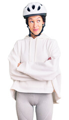 Beautiful brunette young woman wearing bike helmet and sporty clothes smiling looking to the side and staring away thinking.
