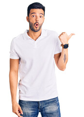 Young handsome hispanic man wearing casual clothes surprised pointing with hand finger to the side, open mouth amazed expression.