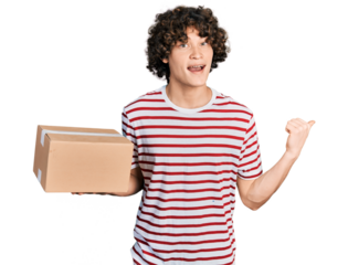 Caucasian teenager holding delivery package pointing thumb up to the side smiling happy with open mouth