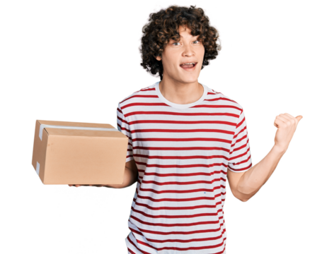 Caucasian teenager holding delivery package pointing thumb up to the side smiling happy with open mouth