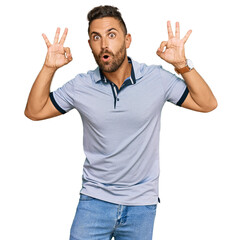 Naklejka premium Handsome man with beard wearing casual clothes looking surprised and shocked doing ok approval symbol with fingers. crazy expression