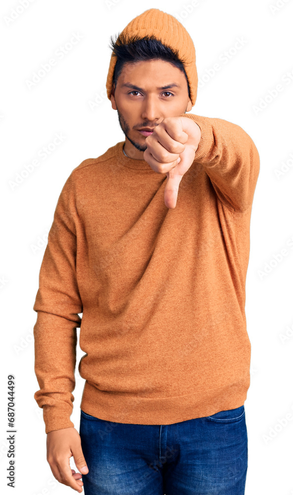 Wall mural handsome latin american young man wearing winter sweater and wool hat looking unhappy and angry show