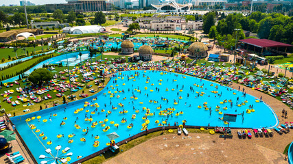 Top view of people relaxing in the pool on yellow inflatable circles and sun beds on the beach