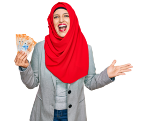 Beautiful hispanic woman wearing islamic hijab holding 10 swiss franc banknotes celebrating victory with happy smile and winner expression with raised hands