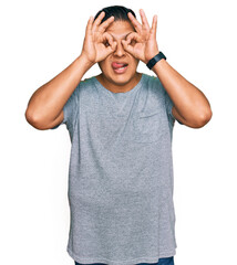 Fototapeta premium Young latin man wearing casual clothes doing ok gesture like binoculars sticking tongue out, eyes looking through fingers. crazy expression.