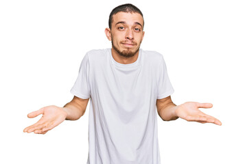 Hispanic young man wearing casual white t shirt clueless and confused expression with arms and...