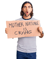 Young handsome man holding mother nature is crying protest cardboard banner scared and amazed with...
