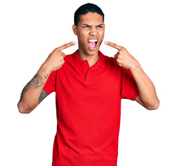 Young hispanic man pointing mouth with fingers angry and mad screaming frustrated and furious, shouting with anger. rage and aggressive concept.